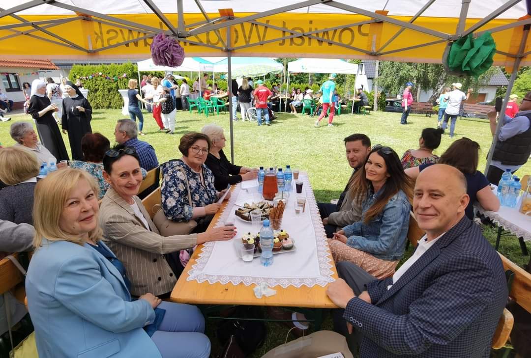 Na zdjęciu widać osoby siedzące przy stole pod namiotem w tle ogród