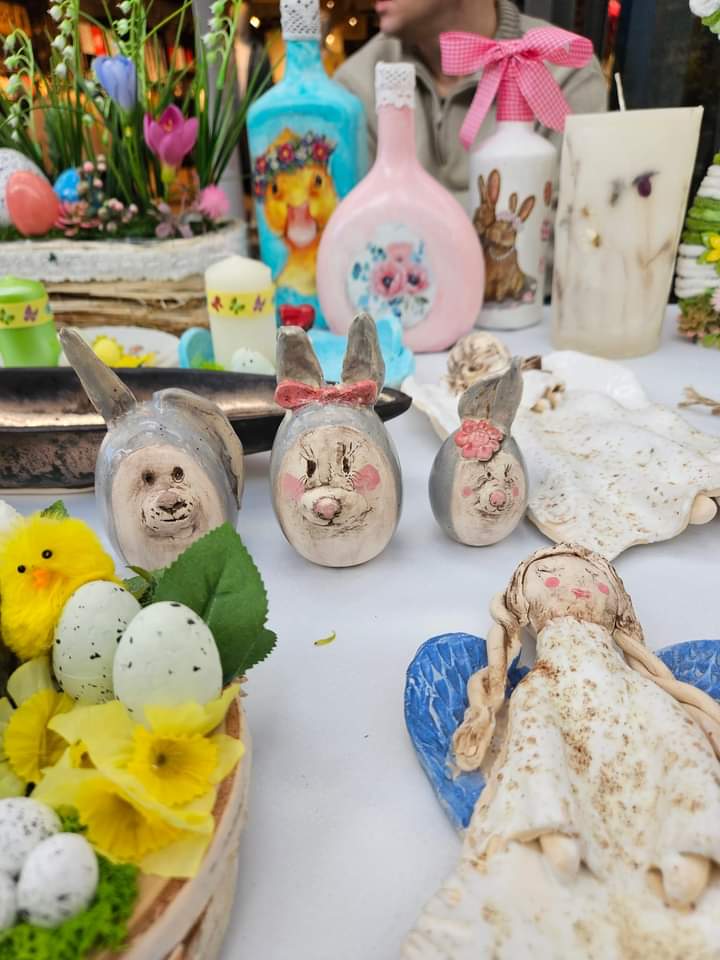 Na zdjęciu widać trzy ceramiczne zajączki i inne ozdoby w tle