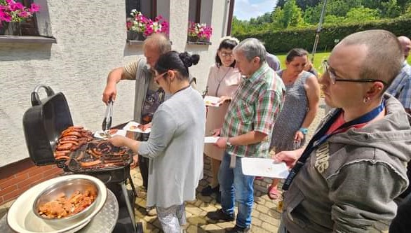 Na zdjęciu widać Uczestników majówki czekających na kiełbaski z grila, które nakłada pracownik Ośrodka.