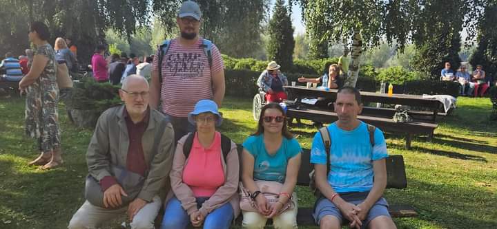 Na zdjęciu widać czwórkę Uczestników siedzących na ławce w tle trawa i drzewa