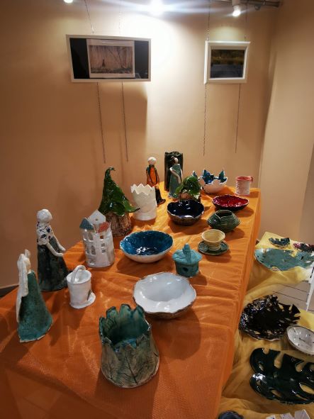 Na stole stoją prace miski, anioły, wazony, domki wykonane przez uczestników Ośrodka z gliny ceramicznej.