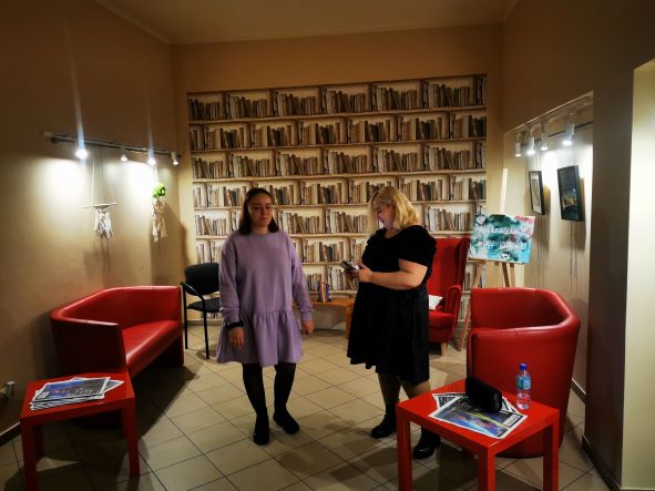 Dwie Uczestniczki śpiewające podczas wernisażu w tle prace Uczestników.