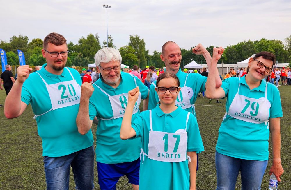 Na zdjęciu trzech mężczyzn i dwie kobiety w turkusowych koszulkach z numerami zawodników trzymają ręce w górze w geście zwycięstwa.