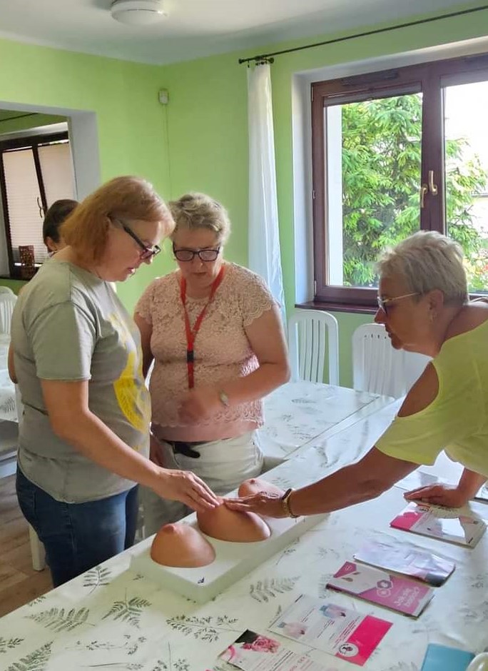 Na zdjęciu widąc dwie kobiety uczące się na sztucznej piersi rozpoznawać występowanie guza w piersi.