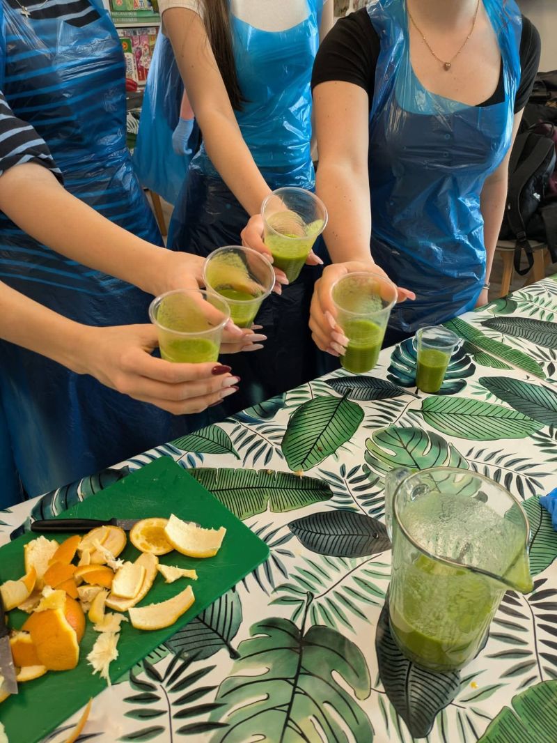 Na zdjęciach widać osoby w fartuchach trzymające szklanki z zielonym smoothie.