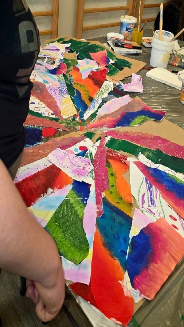 Na zdjęciu widać karton oklejony kolorowymi skrawkami i stojącą obok osobę